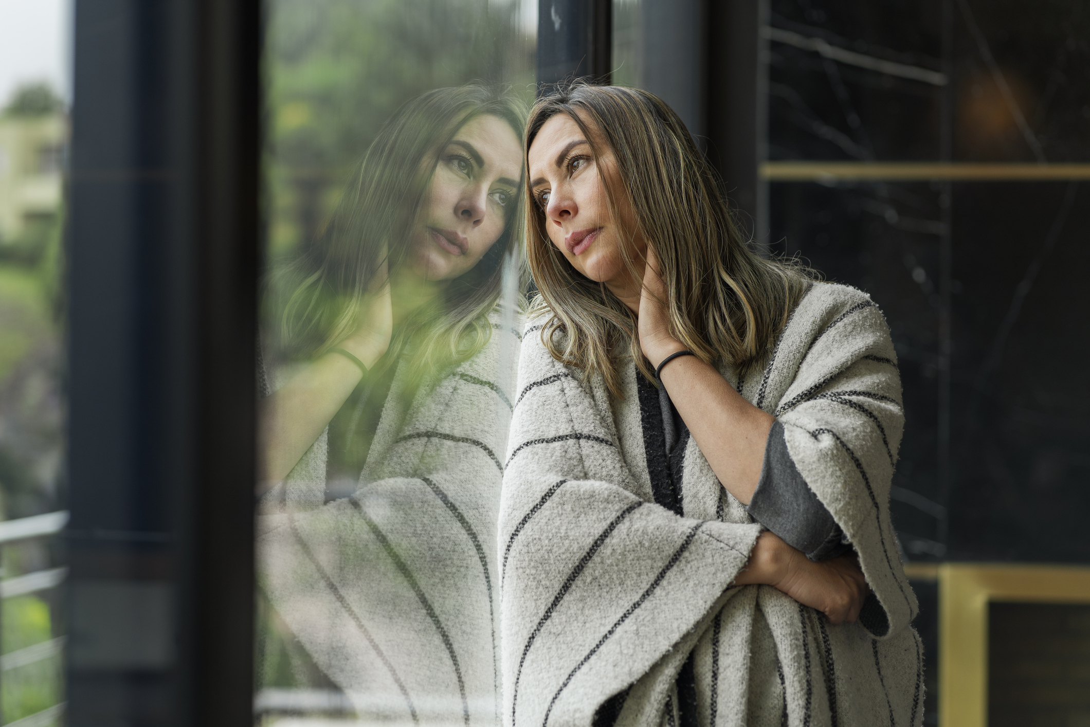 Very bored and sad woman leaning on the window of her house looking away for so much time of isolation